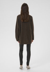 Sötétbarna, oversized pulóver bordás aljjal, fekete, testhez simuló nadrágra húzva, amely lágy textúrát és laza formát mutat.