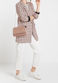 Blazer a scacchi rosa e nero con maniche lunghe, abbinato a jeans bianchi cropped e sneakers bianche. Una borsa a tracolla rosa completa il look.