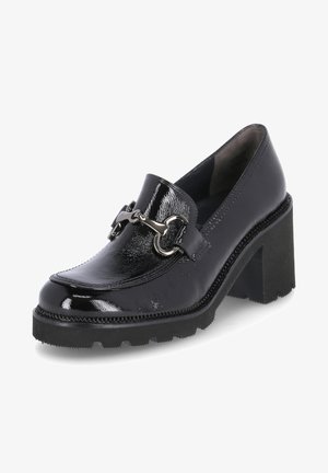 Mocasines de piel negra con un acabado texturizado, que presentan un acento decorativo de cadena metálica y un tacón ancho. Detalle de suela de goma visible.