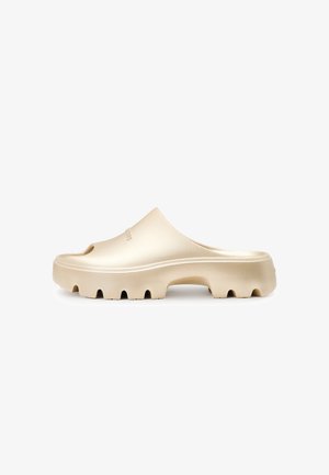 Guld slip-on sko med åben tå, tekstureret gummisål og runde udskæringer langs kanten. Glat finish, moderne design.