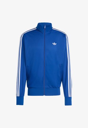 Modrá sieťovaná bežecká bunda s bielymi tromi pruhmi na rukávoch, vysokým golierom, celým zipsom a malým bielym logom na hrudi.