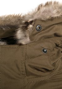 Oliwkowa parka z futrzanym obszyciem z imitacji futra, wyposażona w ciemne metalowe zatrzaski i detale przeszyć, prezentująca gładką teksturę tkaniny oraz uporządkowany kształt.