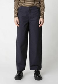 Pantaloni blu navy con una vestibilità ampia, dotati di chiusura a bottone, due tasche frontali e una trama liscia. Abbinati a scarpe chunky nere.