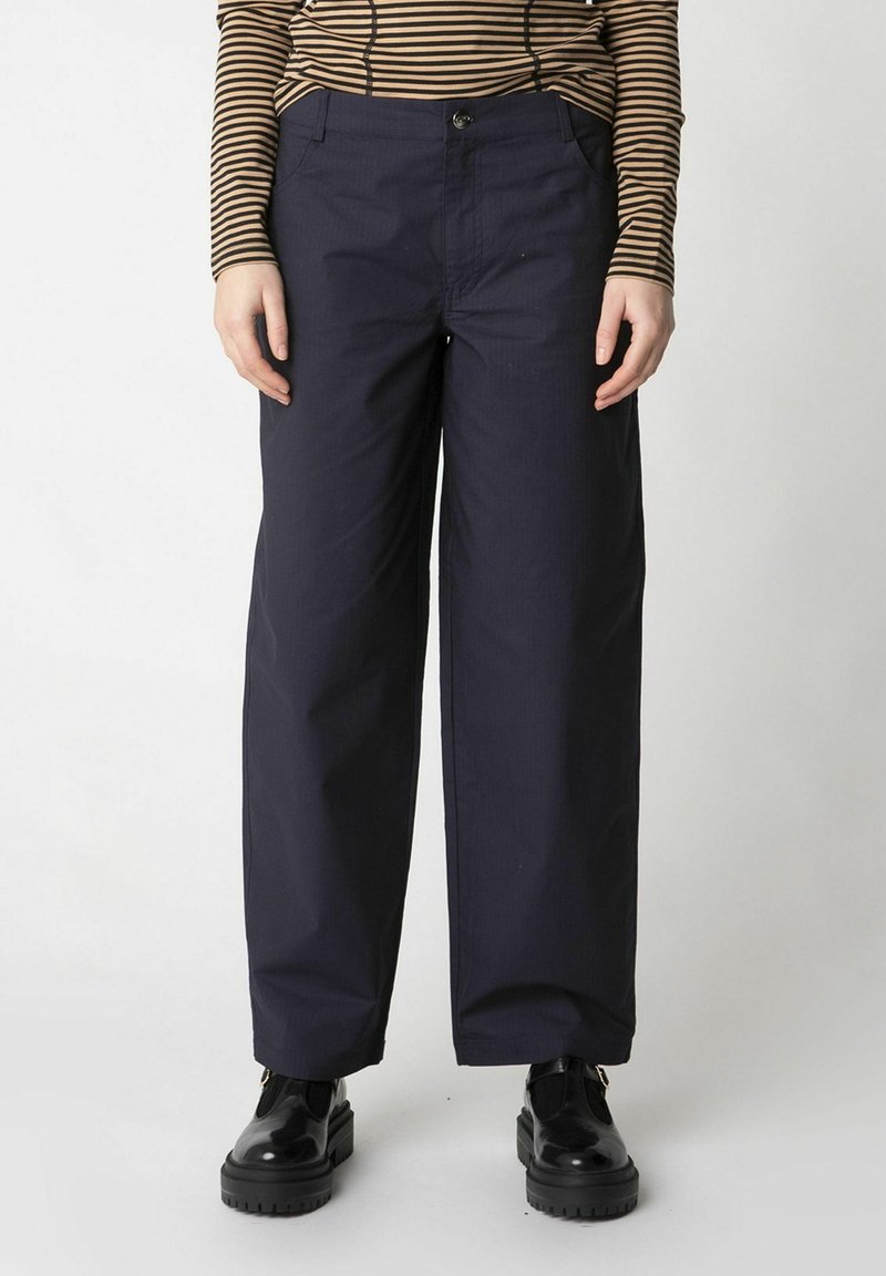 Pantaloni blu navy con una vestibilità ampia, dotati di chiusura a bottone, due tasche frontali e una trama liscia. Abbinati a scarpe chunky nere.