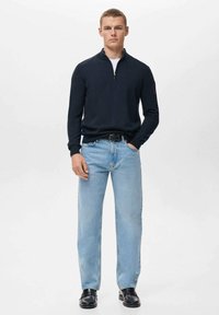 Marineblauer Pullover mit einem Reißverschluss und Stehkragen, kombiniert mit hellblauen, geraden Jeans und schwarzen Lederschuhen. Das Outfit hat eine legere Ästhetik.