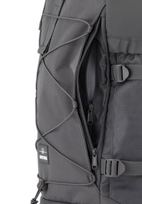 Mochila gris con tejido texturizado, que cuenta con un compartimento con cremallera, detalles de cordón elástico y hebillas ajustables para un cierre seguro.