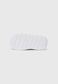 Semelle de sneaker en caoutchouc blanc avec des nervures texturées et un design minimaliste, arborant un profil bas et un branding subtil.