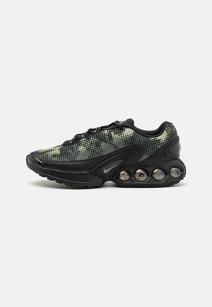 Des baskets Nike noires présentent un dessus en maille verte texturée, une semelle noire élégante et des éléments de coussinage à air visibles en forme courbée.