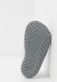 Scarpa atletica leggera con suola in gomma grigia, presenta un motivo di battistrada ondulato e dettagli in rosa e bianco nel design superiore.