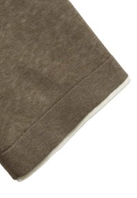 Hnědá látka s texturovaným povrchem, s bílým lemem podél spodního okraje. Design má mírně nepravidelný vzor.