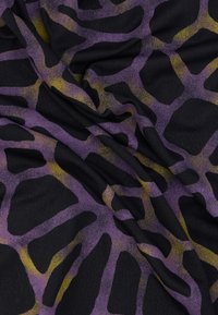 Μωβ και μαύρο ύφασμα με υφή εμπριμέ ζώου και κίτρινα στοιχεία, που πέφτει σε απαλές πτυχώσεις.