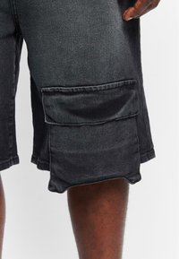 Shorts cargo din denim negru, cu o croială lejeră, prezentând un buzunar lateral mare, tiv brut și o textură subtilă.
