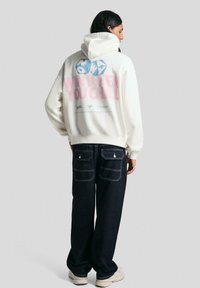 Felpa bianca con una grande grafica sul retro in blu e rosa. Abbinata a pantaloni in denim scuro con due tasche posteriori.
