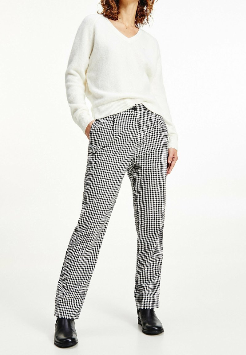 Pull blanc à col en V et pantalon à motif pied-de-poule noir et blanc avec une coupe décontractée. Le pantalon comporte des poches latérales et une fermeture à bouton.