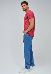 T-shirt rossa di cotone, maniche corte, abbinata a jeans blu in denim. Sneakers bianche completano l'outfit, con dettagli minimi sugli indumenti.