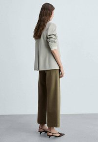 Blazer oversized gris clair avec manches retroussées, associé à un pantalon vert olive à jambes larges. Des chaussures noires à bout pointu complètent la tenue.
