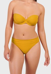 Žuti bikini set koji se sastoji od bandeau gornjeg dijela s oblikovanim košaricama i visokog donjeg dijela, oba izrađena od glatkog, rastezljivog materijala s mat završnom obradom.