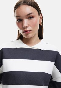 Gestreifter Pullover in Marineblau und Weiß, aus einem weichen Material gefertigt. Mit Kragen und lässigem Schnitt. Einfaches horizontales Muster.