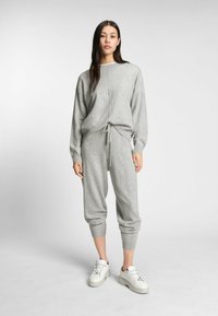 Grauer Strickpullover mit überschnittenen Schultern und verstellbarem Kordelzug an der Taille, kombiniert mit passenden grauen Jogginghosen, beide mit gerippten Bündchen.