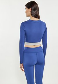 Blauwe sportoutfit bestaande uit een lange mouw crop top en hoge taille legging. Gemaakt van gladde stof met een contrasterende lichtgrijze band.