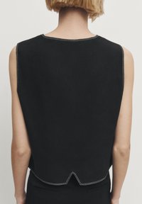 Schwarzes ärmelloses Top aus Denim, mit einem gewellten Saum und kontrastierendem weißen Stich entlang des Ausschnitts und der Armausschnitte.