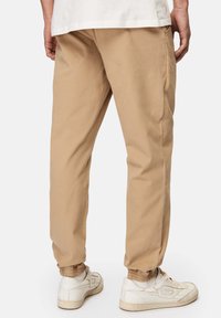 Khakihosen mit elastischen Bündchen, aus weichem Baumwollmaterial, mit Seitentaschen und einem lockeren Schnitt. Kombiniert mit weißen Turnschuhen.