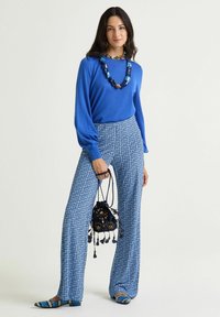 Top blu a maniche lunghe con scollo rotondo, abbinato a pantaloni a gamba larga con motivo nei toni del blu, con collana di perline e borsa.