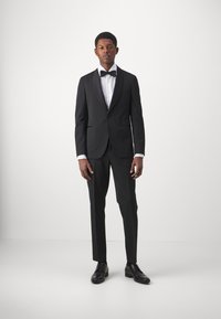 Sort smoking med satinspidsklap, hvid skjorte, butterfly og skræddersyede bukser. Sko af sort læder fuldender det formelle look.
