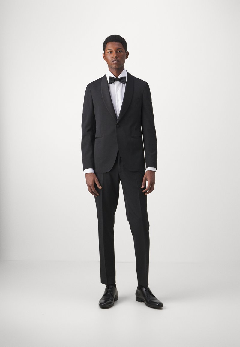 Sort smoking med satinspidsklap, hvid skjorte, butterfly og skræddersyede bukser. Sko af sort læder fuldender det formelle look.
