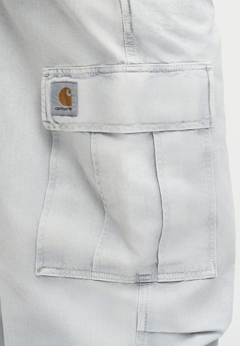 Hellgraue Arbeitshose mit Tasche und Klappe sowie einem Carhartt-Logoaufnäher, der in der oberen linken Ecke der Klappe angenäht ist.