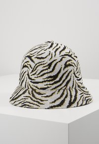 Gorra de cubo con un patrón de rayas de cebra en negro, blanco y amarillo. Fabricada con tela texturizada, presenta una corona redondeada y un ala ancha.