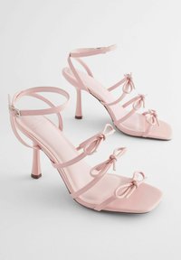 Rosa High-Heels-Sandalen aus glänzendem Material, mit mehreren Riemen und dekorativen Schleifen. Quadratförmige Zehen und schlanke Absätze.
