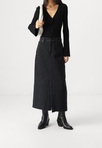 Black ribbed bodysuit with a deep V-neck and long bell sleeves, paired with a high-waisted black denim skirt featuring a front slit.