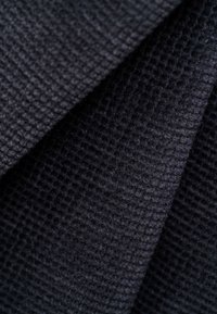 Textured black fabric featuring a woven pattern; the surface appears slightly fuzzy, with folds revealing depth and dimension.