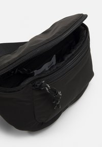 Juodas nailono maišelis su užtrauktuku, turintis tekstūruotą paviršių ir reguliuojamą dirželį, demonstruojantis elegantišką, kompaktišką dizainą.