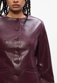Fialová kožená bunda s okrúhlym golierom, zapínaním na päť gombíkov a dvoma prednými vreckami s hladkým povrchom.