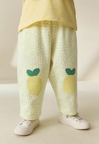 Ljusgula, löst sittande byxor med prickigt grönt mönster och citronformade applikationer på knäna. Kombinerade med vita sneakers.