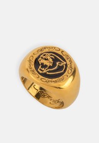 Złota obrączka z gładką, zaokrągloną obręczą; w centrum znajduje się czarna głowa lwa, otoczona wygrawerowanym napisem "Ed Hardy."