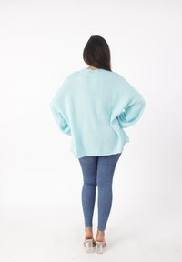 Helles blaues, oversized Sweatshirt mit weicher Textur, geripptem Ausschnitt und überschnittenen Schultern, kombiniert mit enganliegenden blauen Jeans und transparenten High Heels.