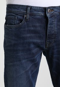 Mörkblå denimjeans med en klassisk design, femfickor, synlig sömnad och en metallknapp som stängning i midjan.