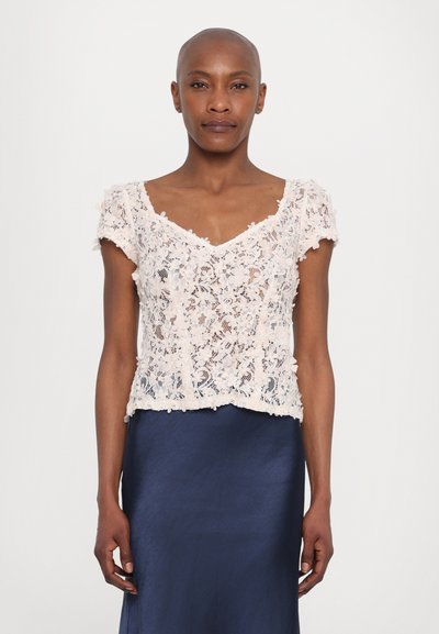 Haut en dentelle rose clair avec des manches courtes et un col en V, orné de motifs floraux et d'un ourlet en dentelle, porté sur une jupe en satin bleu marine.