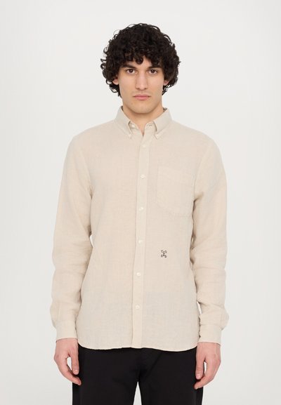 Lys beige linned skjorte med lange ærmer, knap-ned krave, brystlomme og et lille sort logo på brystet. Tekstureret stof.