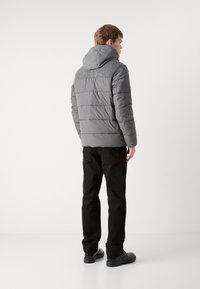 Giacca imbottita grigia con cappuccio, caratterizzata da un colletto in maglia e una texture liscia, abbinata a pantaloni neri e scarpe nere.