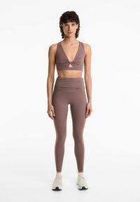 Set de îmbrăcăminte sport în două piese, de culoare mauve, compus dintr-un top scurt cu detaliu răsucit și colanți cu talie înaltă, cu textură strânsă.