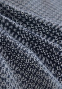 Tissu bleu foncé avec de petits motifs géométriques blancs, présenté en plis doux mettant en valeur la texture et les détails du motif.