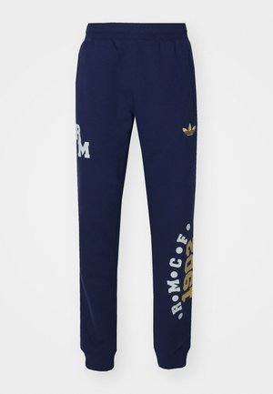 Navy blue sweatpants with an elastic waistband. Features a gold Adidas logo and white text patterns, made of soft fabric. Adjustable cuffs.