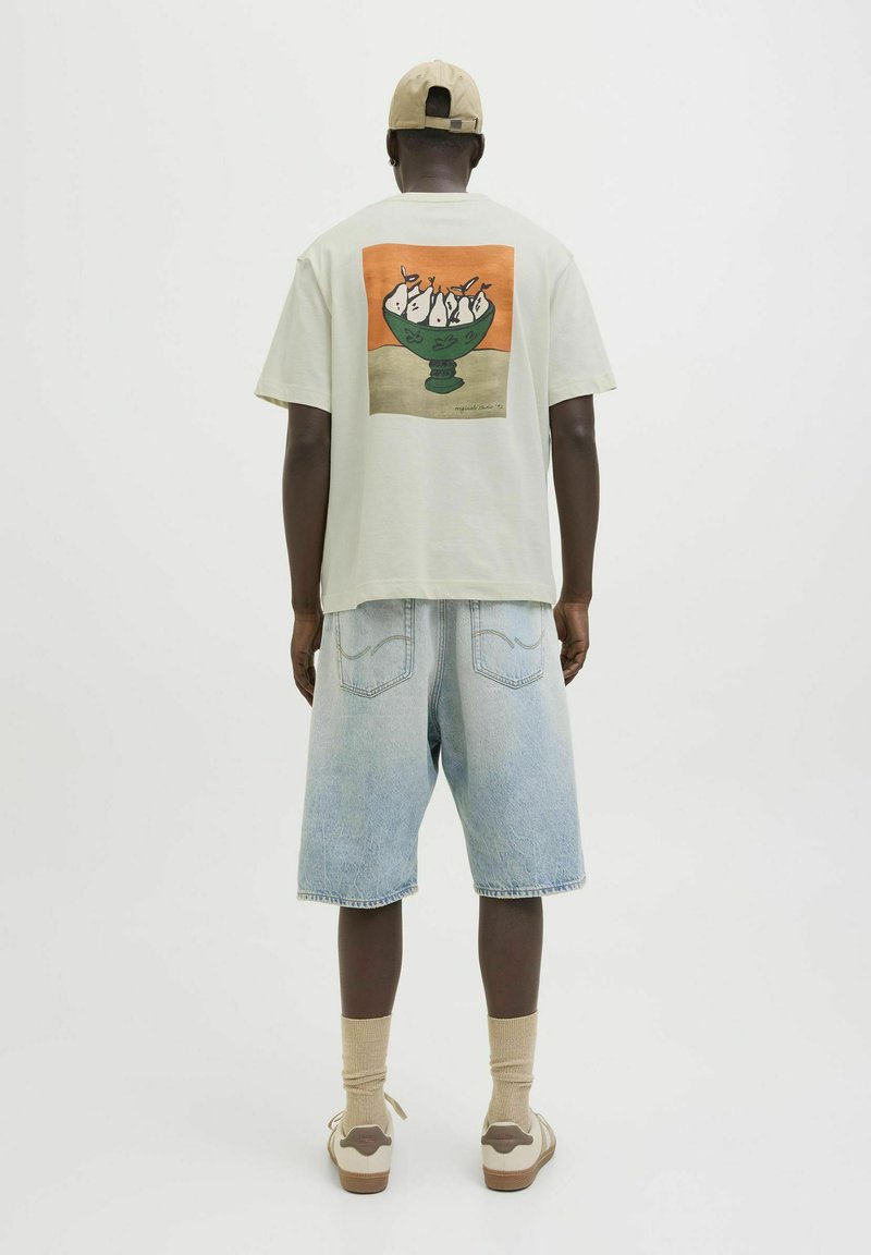 Camiseta de algodón verde claro con un gráfico colorido de un bol de helado en la espalda. Lleva puesta con pantalones cortos de mezclilla azul claro y calcetines beige.