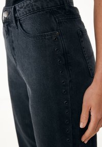 Vaqueros de mezclilla negra con cintura alta, detalles de broche lateral y un clásico diseño de cinco bolsillos con una textura suave.