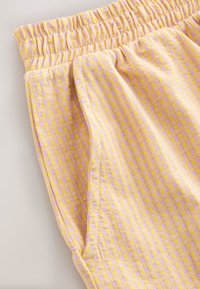 Pantalon à taille élastique à carreaux jaunes et roses avec détail de poche latérale, présenté sur un fond clair.