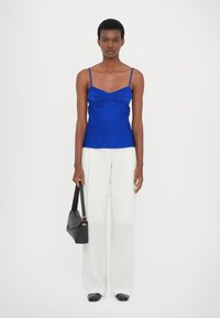 Top senza maniche blu royal con corpo aderente e dettagli arricciati, abbinato a pantaloni bianchi larghi e una borsa a tracolla nera.
